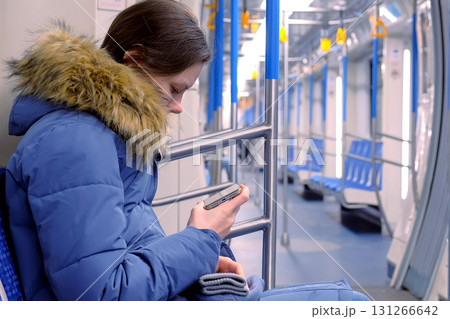 Woman goes in an empty subway car and watches a video on her smartphone. Side view. Woman goes in an empty subway car and watches a video on her smartphone. Side view. 131266642