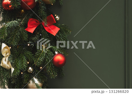 Christmas tree branches with red balls and a golden bow on a green background 131266820