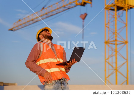 Construction engineer using laptop at building site with crane in background Construction engineer using laptop at building site with crane in background 131268623