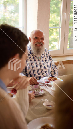 Smiling elderly man with beard enjoying family dinner at table Smiling elderly man with beard enjoying family dinner at table 131268976
