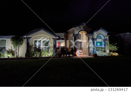 Festive front yard with a big inflatable pumpkin and blue pumpkin faces projected on windows. Nighttime holiday display on a suburban home. Festive front yard with a big inflatable pumpkin and blue pumpkin faces projected on windows. Nighttime holiday display on a suburban home. 131269417