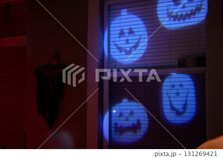 Smiling pumpkin faces are projected in blue light onto a home window at night. Festive Halloween decoration with a spooky yet cheerful mood. Smiling pumpkin faces are projected in blue light onto a home window at night. Festive Halloween decoration with a spooky yet cheerful mood. 131269421