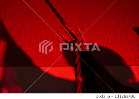 A bony hand holds a braided rope beside a wall in intense red light. Spooky Halloween detail with strong shadows and eerie mood at night. 131269430