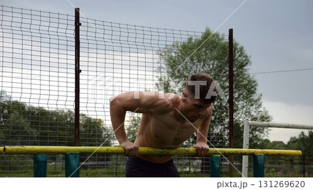 Male shirtless athlete doing push ups on parallel bars at nature. Strong sporty man exercising at sports ground. Young sportsman training hard outdoor. Concept of active sportive lifestyle. Slow mo Male shirtless athlete doing push ups on parallel bars at nature. Strong sporty man exercising at sports ground. Young sportsman training hard outdoor. Concept of active sportive lifestyle. Slow mo 131269620
