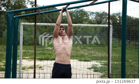 Young muscular sportsman doing pull ups at sports ground. Athletic guy exercising outdoor. Strong sporty man working out at summer nature. Concept of healthy and active lifestyle. Slow motion 131269637