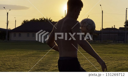 Young man juggling soccer ball on stadium at sunset. Professional footballer kicking ball at green field. Sportsman practicing tricks at meadow with sunlight at background. Freestyle football 131269712
