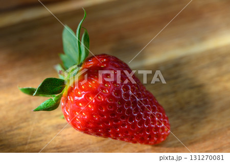 Freshly picked strawberry resting on a wooden surface captured in soft natural 131270081