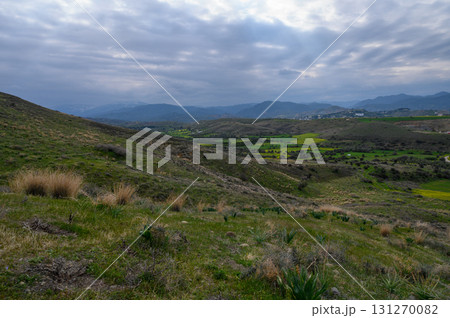 Rolling green hills under a moody sky with scattered clouds at dusk in a rural 131270082