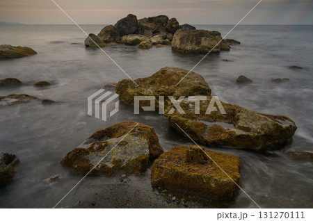 Rocky shoreline at dusk with gentle waves kissing the coast and a serene sky 131270111