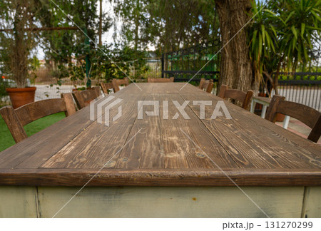 Long wooden table set for gathering in a peaceful outdoor garden during a sunny Long wooden table set for gathering in a peaceful outdoor garden during a sunny 131270299
