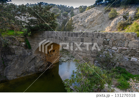Ancient stone bridge nestled among lush greenery beside a tranquil river in Ancient stone bridge nestled among lush greenery beside a tranquil river in 131270318