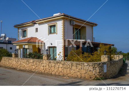 Charming two-story house with stone wall and greenery under the clear blue sky Charming two-story house with stone wall and greenery under the clear blue sky 131270754