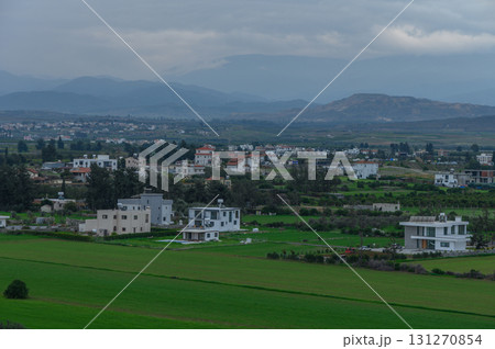 Green fields and modern homes amidst a cloudy sky in a tranquil rural landscape Green fields and modern homes amidst a cloudy sky in a tranquil rural landscape 131270854