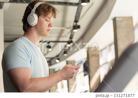 Athlete man with cellphone or mobile phone running track on treadmill at gym. Warming up and cardio training. Work out at fitness center. Close up. 131271877