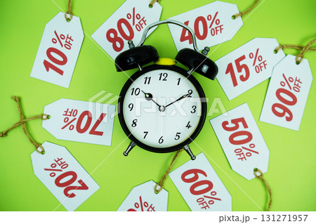 Clock surrounded by various discount tags with percentages like 10%, 20%, 30%, up to 90% off, set against a bright green background 131271957