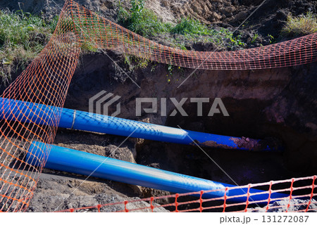 Stacked blue pipes resting in a field near a forest during daylight 131272087