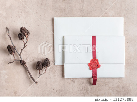 White envelope sealed with red ribbon and on beige stone background 131273899