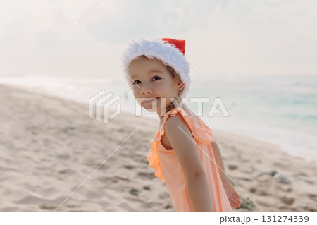 Little girl in ocean beach with Christmas hat. Happy smiling girl Little girl in ocean beach with Christmas hat. Happy smiling girl 131274339