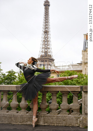 Ballerina performing elegant dance pose in black tutu with Eiffel Tower in Paris 131274412