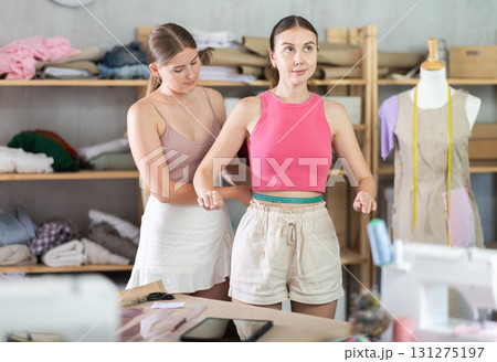 Young seamstress takes body measurements from adult woman 131275197