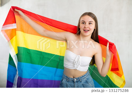 Positive young teen girl in casual clothes holds unfurled flag of LGBT in hands raised above head Positive young teen girl in casual clothes holds unfurled flag of LGBT in hands raised above head 131275286