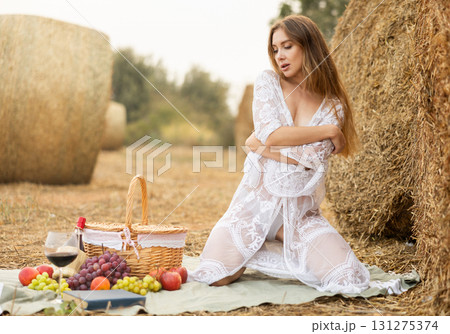 Sexy young woman in white transparent dress sitting near haystack relaxing on romantic picnic Sexy young woman in white transparent dress sitting near haystack relaxing on romantic picnic 131275374