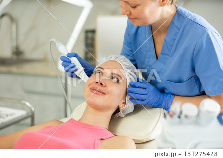 Professional cosmetologist doing ultrasonic facial cleansing for young woman in spa center. Non-invasive skin rejuvenation Professional cosmetologist doing ultrasonic facial cleansing for young woman in spa center. Non-invasive skin rejuvenation 131275428