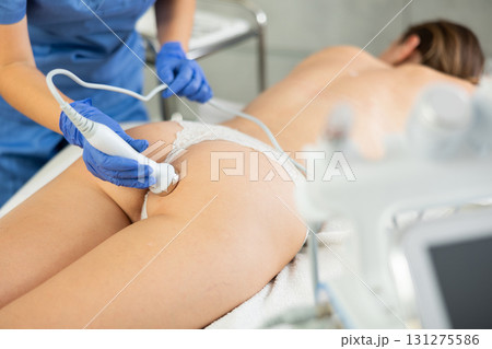 Adult woman cosmetologist gives ultrasonic massage of butt to young woman 131275586