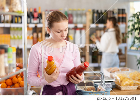 Young girl buyer chooses tomato and peach juices Young girl buyer chooses tomato and peach juices 131275601