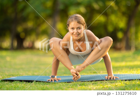Girl performing shoulder-pressing pose Bhujapidasana in summer park Girl performing shoulder-pressing pose Bhujapidasana in summer park 131275610