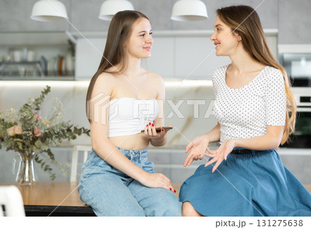 Kind middle-aged mother talking to young daughter sitting on kitchen-table 131275638