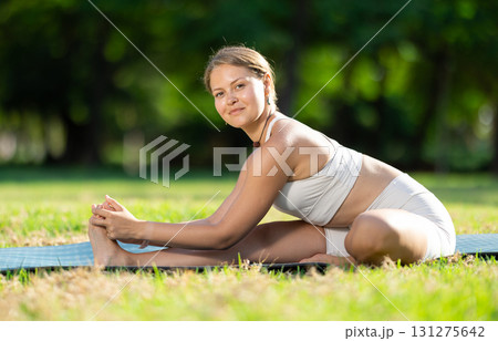 Girl in park on green grass of lawn performs Pashchimottanasana Girl in park on green grass of lawn performs Pashchimottanasana 131275642