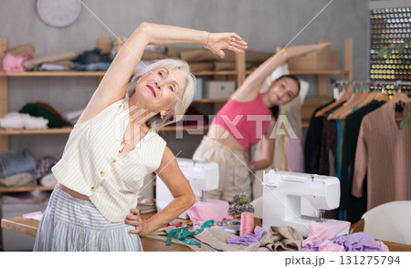 Elderly and adult women doing warm-up exercises in sewing workshop Elderly and adult women doing warm-up exercises in sewing workshop 131275794