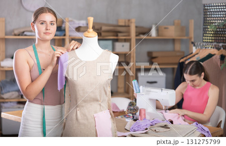 young dressmaker stands near a mannequin with a seamstress in the background 131275799