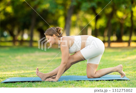 Girl doing Half Splits Pose on mat in summer park 131275802