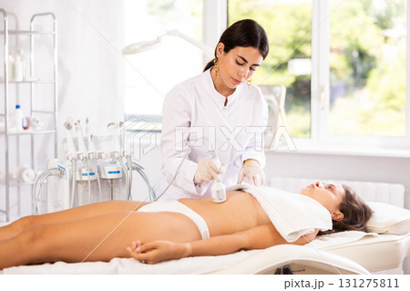Cosmetologist performing cryotherapy procedure with cooling hammer on female client belly 131275811