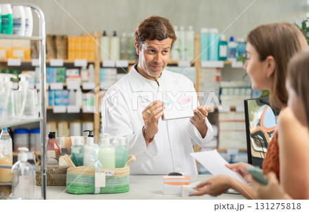 Mother and daughter choose pills in drugstore. Male pharmacist offers to buy pills Mother and daughter choose pills in drugstore. Male pharmacist offers to buy pills 131275818