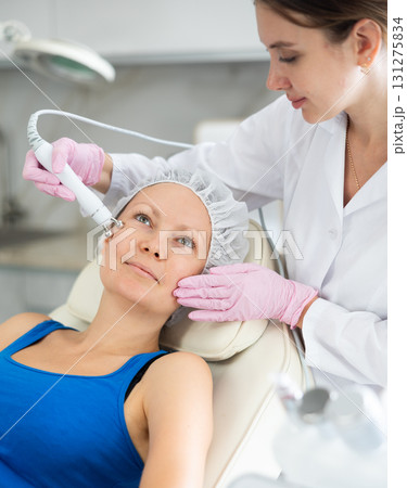 Young female cosmetologist doing microcurrent procedure to adult woman 131275834
