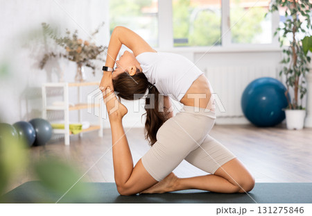 Young woman yoga trainer performing king pigeon pose on black rug Young woman yoga trainer performing king pigeon pose on black rug 131275846