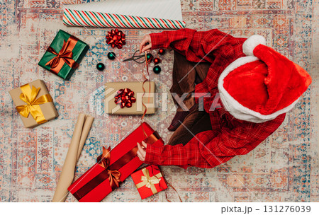woman in hat sits on cozy rug surrounded gift boxes, wrapping Christmas presents woman in hat sits on cozy rug surrounded gift boxes, wrapping Christmas presents 131276039