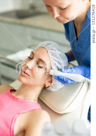 Young girl getting facial rf-lifting procedure of smoothes wrinkles and tightens skin on face in beauty salon. Concept of professional cosmetology 131276419