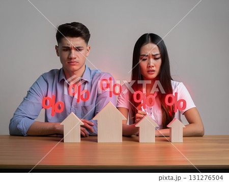 Stressed young couple looking at miniature house models with floating interest rate percentages, burden of high mortgage interest rates 131276504