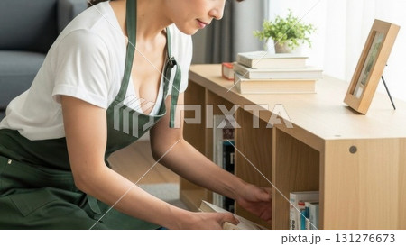 リビングの本棚を整理整頓するエプロン姿の若い女性 131276673