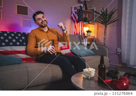 Enjoying a relaxed evening on a cozy sofa adorned with flags and surrounded by snacks while watching a game 131276864