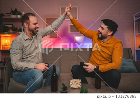 Friends joyfully celebrate gaming victory in a cozy living room during a late night gathering filled with laughter and camaraderie Friends joyfully celebrate gaming victory in a cozy living room during a late night gathering filled with laughter and camaraderie 131276865