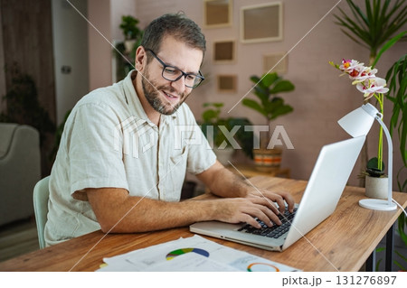 Smiling man working on laptop in cozy home office 131276897