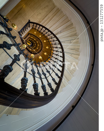 Spiral staircase with ornate wrought iron railing and warm pendant lights viewed from above 131277559