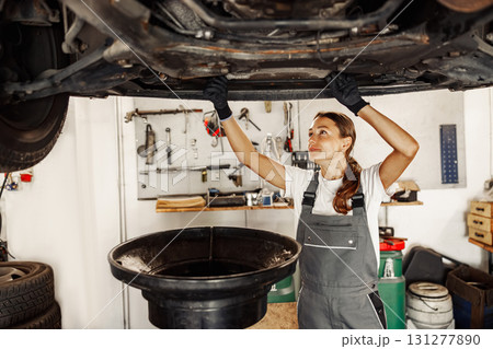 A Skilled Female Mechanic Engaged in Detailed Work Underneath a Car in a Busy Garage A Skilled Female Mechanic Engaged in Detailed Work Underneath a Car in a Busy Garage 131277890