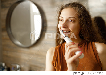 A Smiling Woman Brushing Her Teeth in a Modern Bathroom Setting with Stylish Decor and Fixtures A Smiling Woman Brushing Her Teeth in a Modern Bathroom Setting with Stylish Decor and Fixtures 131277943