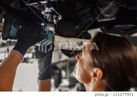 Skilled Mechanic Working Hard Underneath a Vehicle Using Various Power Tools for Repair Skilled Mechanic Working Hard Underneath a Vehicle Using Various Power Tools for Repair 131277951